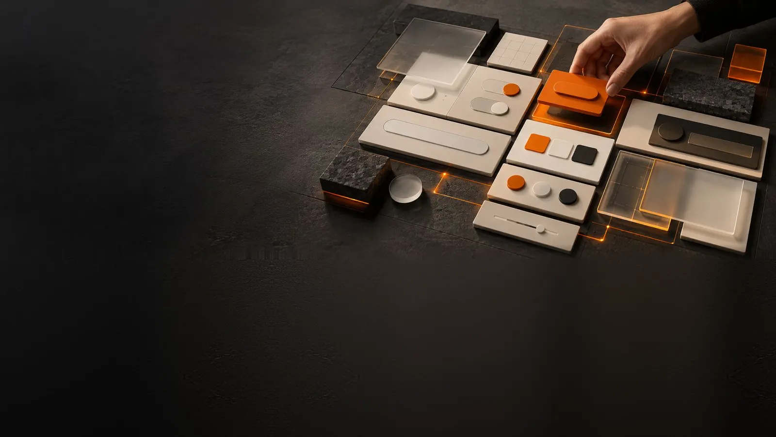 A hand placing an orange interface tile among stone and frosted-glass component tiles laid out on a dark surface