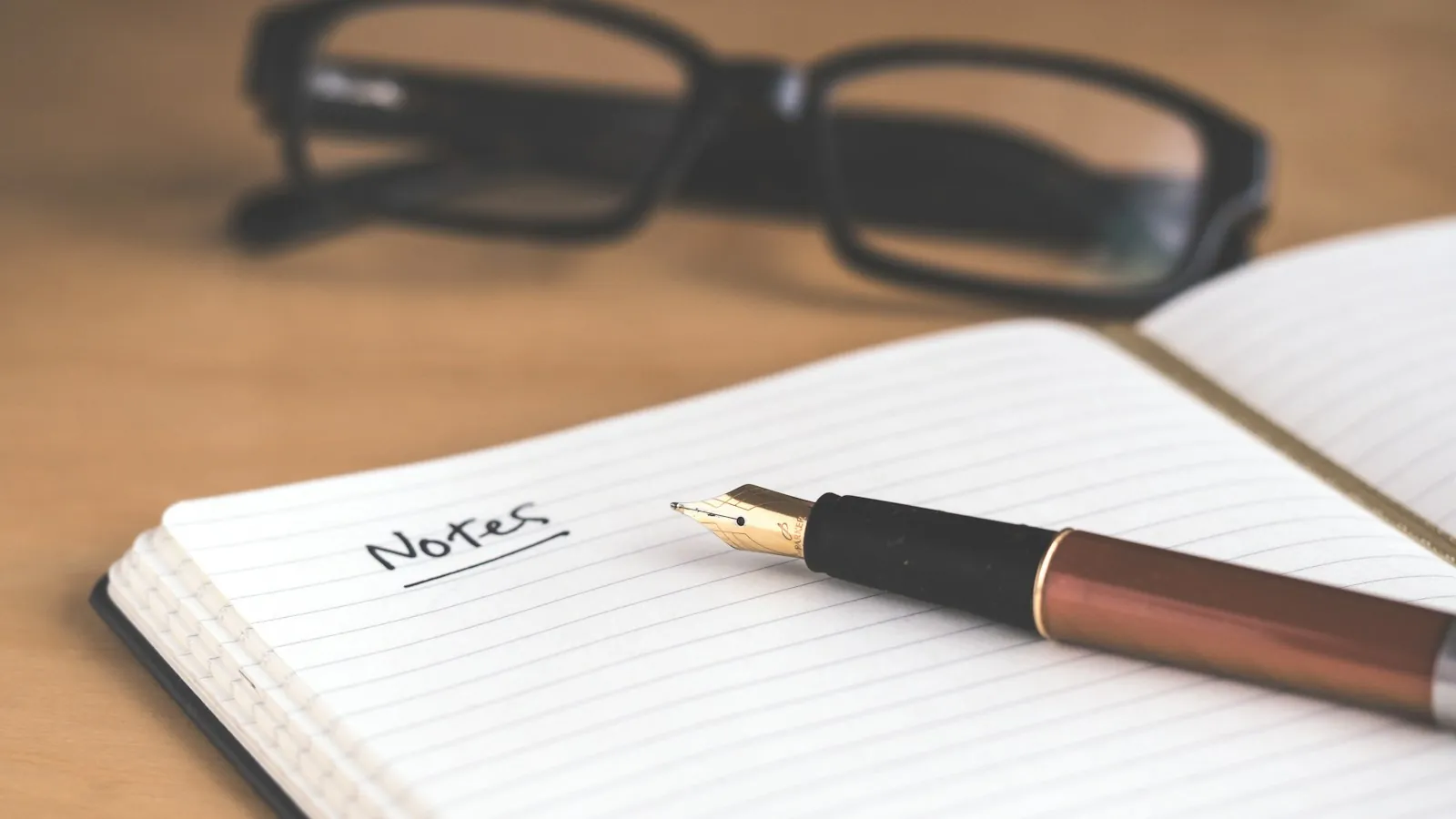Glasses resting on an open notebook with a pen